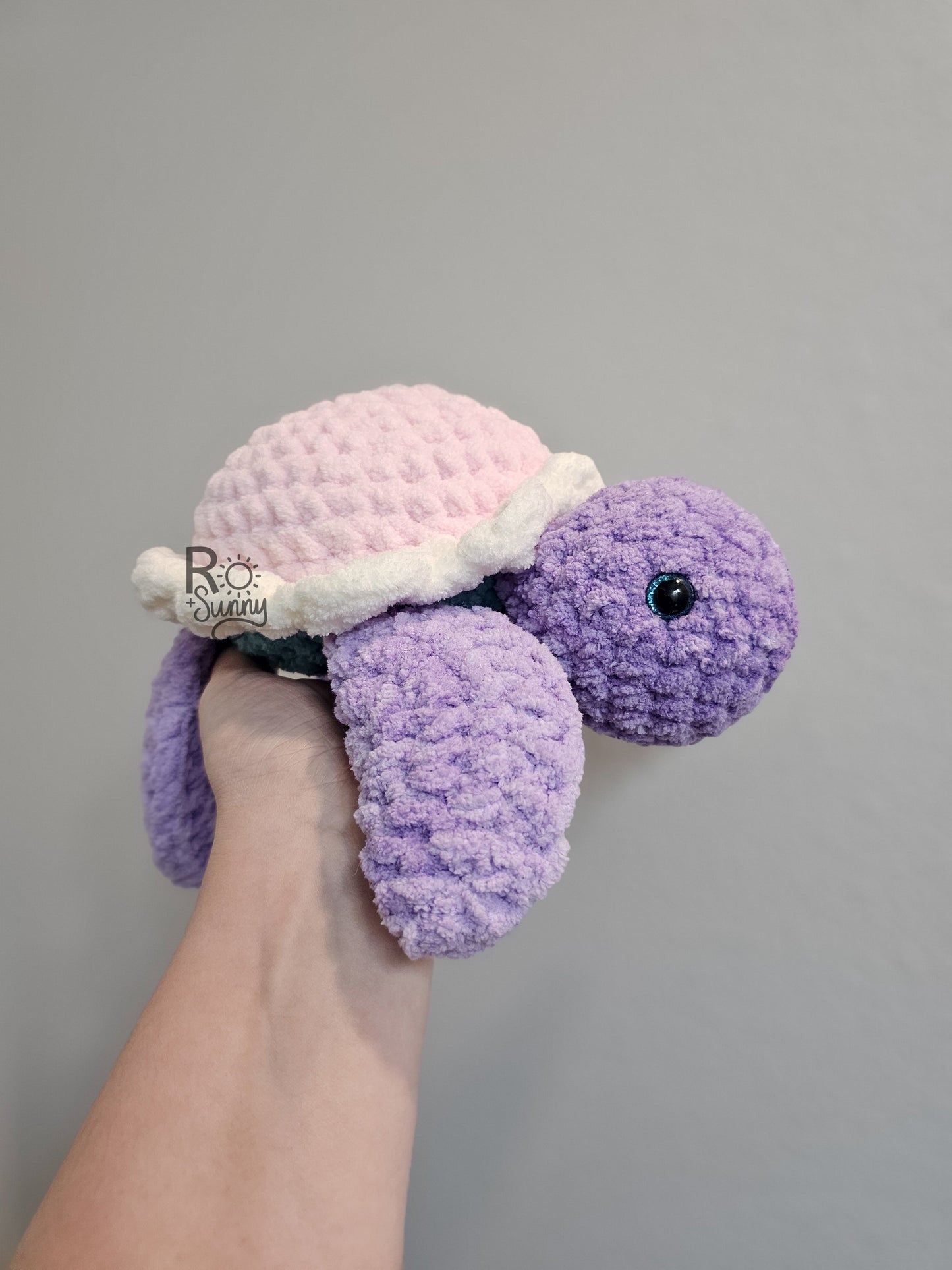 Cotton Candy, Side Profile - Crochet sea turtle with a purple body and light pink shell with that has a white ruffle. The belly of the turtle is a light teal color. 