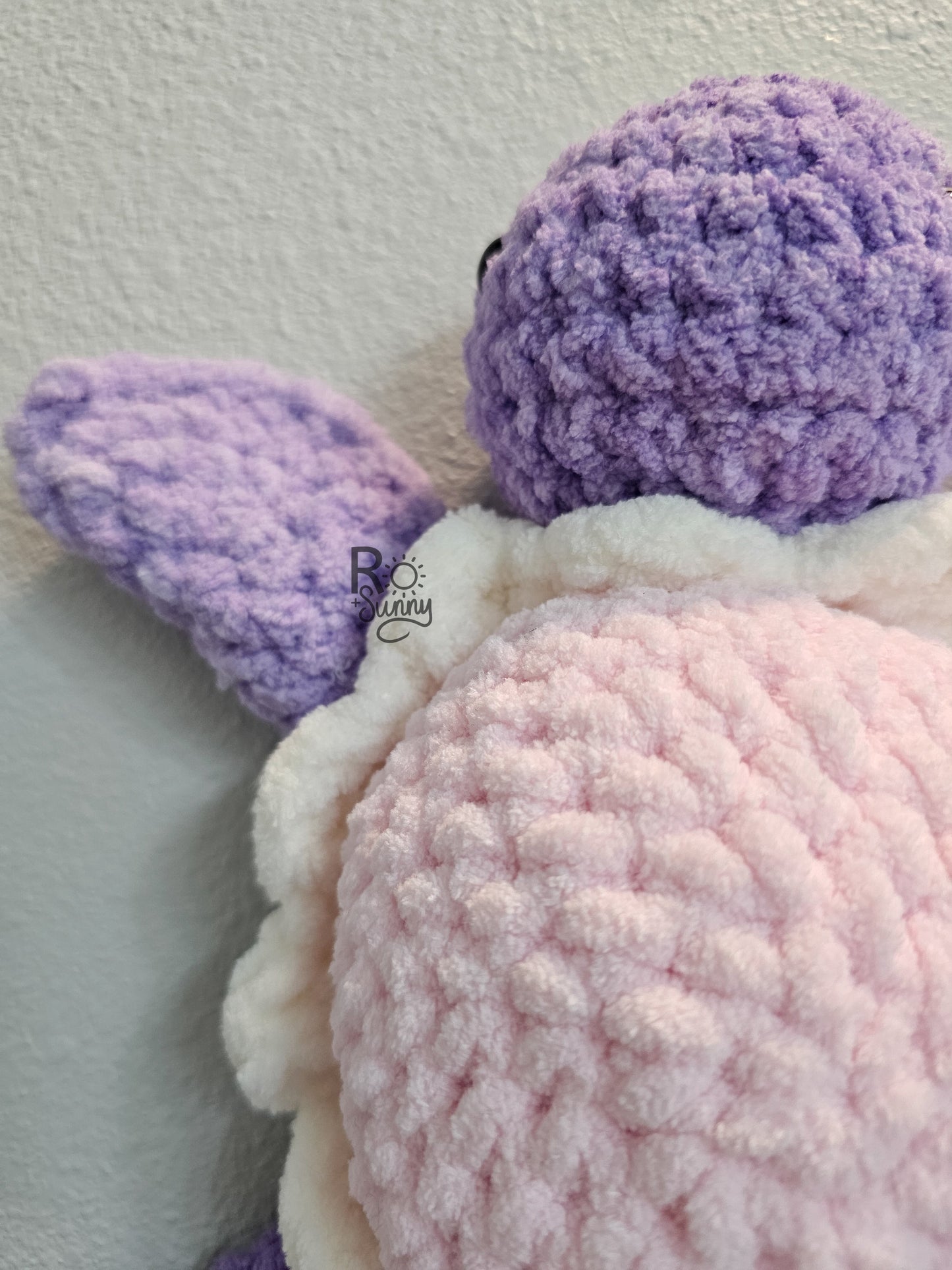 Cotton Candy, Closeup  - Crochet sea turtle with a purple body and light pink shell with that has a white ruffle. The belly of the turtle is a light teal color. 