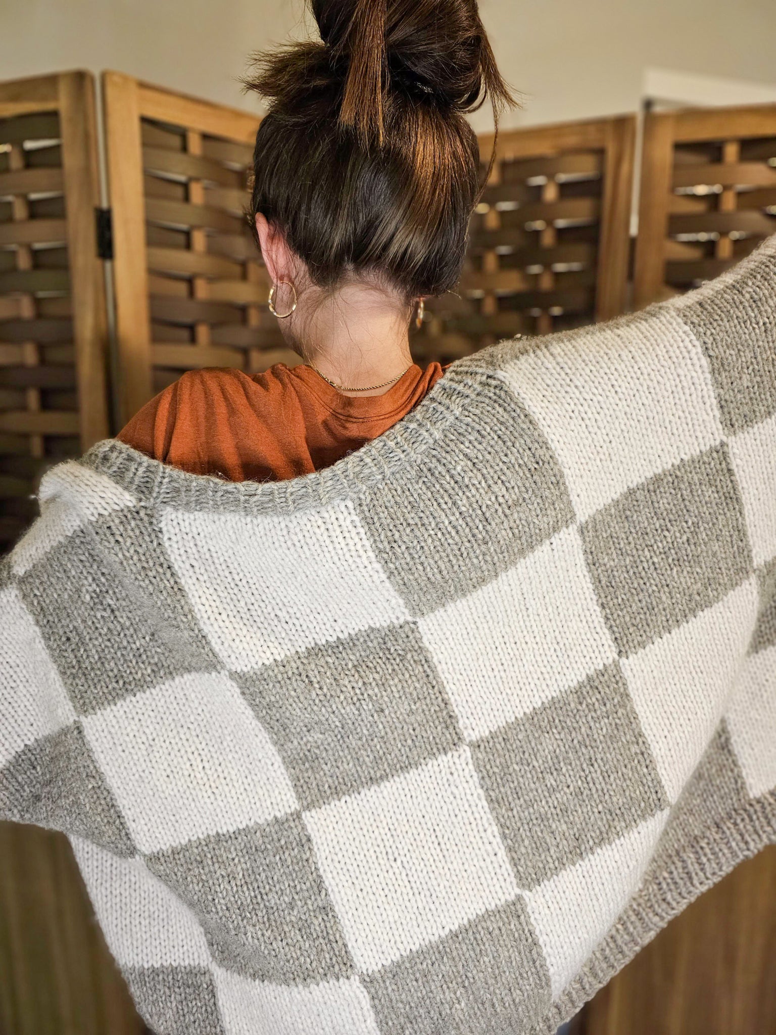 Women wearing oversized handknit cardigan. The design features large checkered blocks of white and gray. 