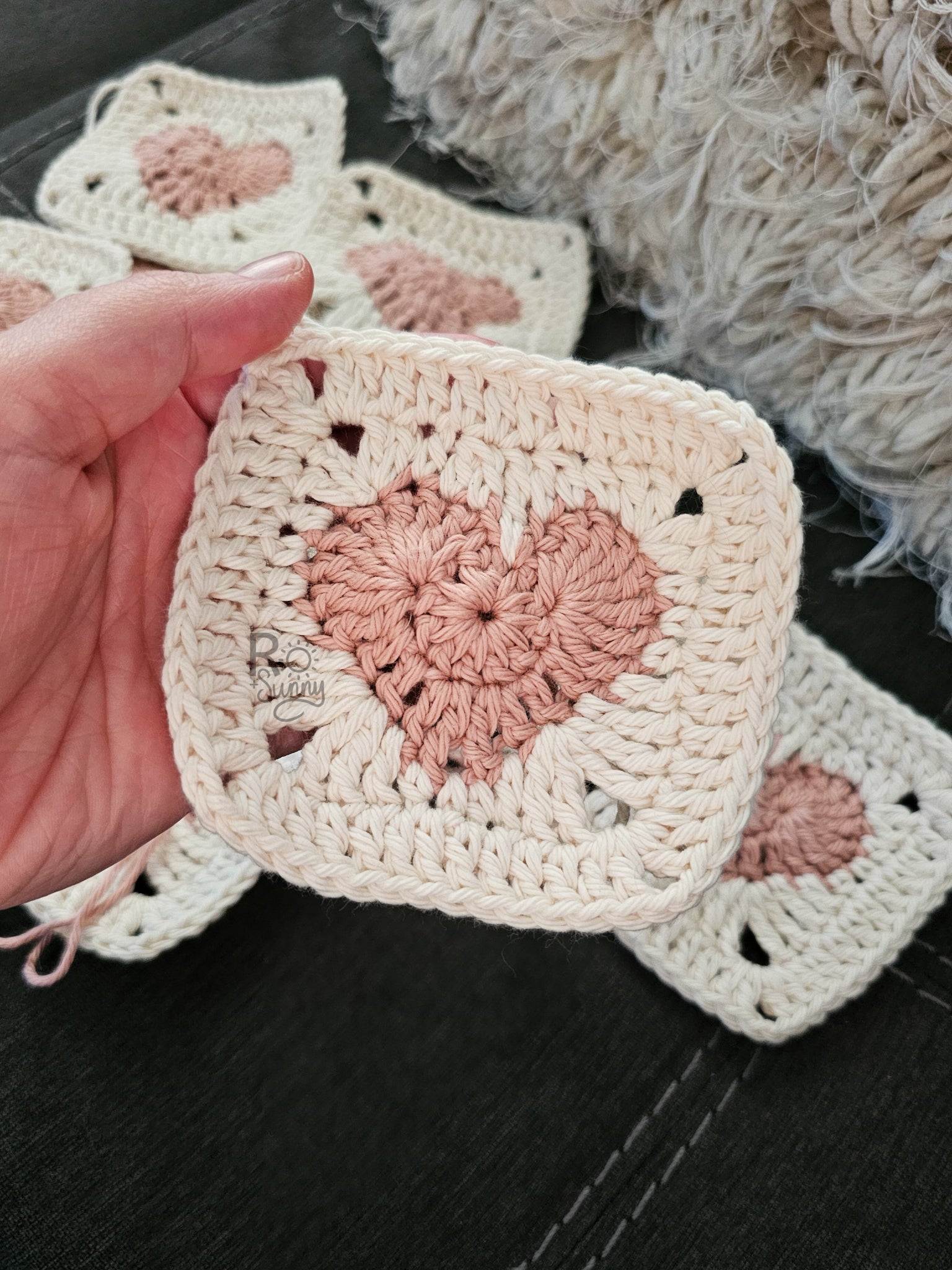 Hand holding heart granny square in pink and white.